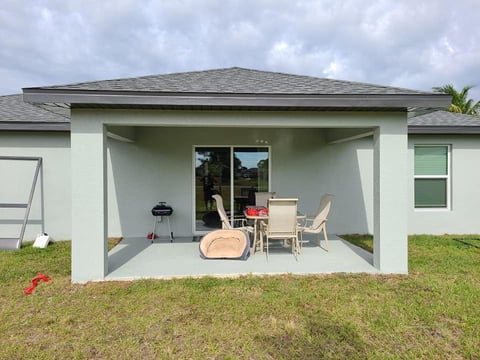 Single-story house with covered patio featuring comfortable outdoor furniture and grill under a gray roof