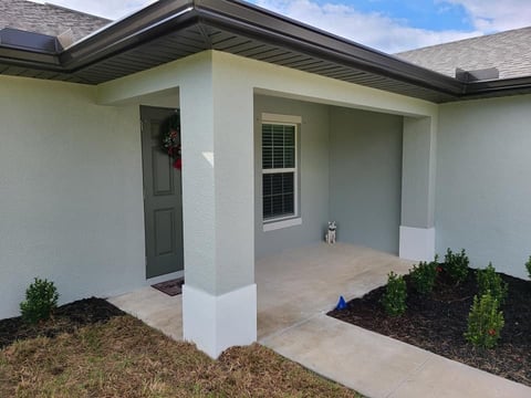 Modern home entry with white columns, covered porch, dark green door, and landscaped front beds
