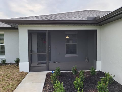 Modern home exterior with gray sliding glass patio doors, white walls, landscaped garden beds, and concrete walkway