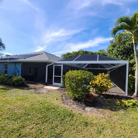 Modern single-story house with blue exterior, black pergola, and green lawn under clear blue sky