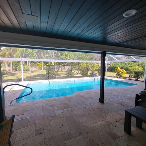Indoor swimming pool with blue water under a dark ceiling, viewed through large windows overlooking landscaped grounds