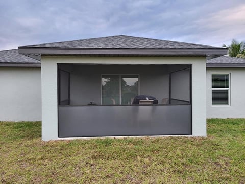 Modern white and gray screened outdoor patio structure attached to residential home with gray roof and green lawn